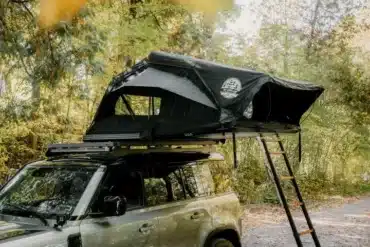 Geöffnetes Go Overland Voyage Hybrid-Dachzelt auf einem Geländewagen mit Leiter und seitlichen Fenstern im Wald.