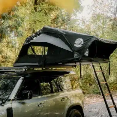 Geöffnetes Go Overland Voyage Hybrid-Dachzelt auf einem Geländewagen mit Leiter und seitlichen Fenstern im Wald.