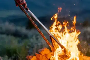 Donkey Tong Grillzange hält Holz über offenem Lagerfeuer im Outdoor-Einsatz