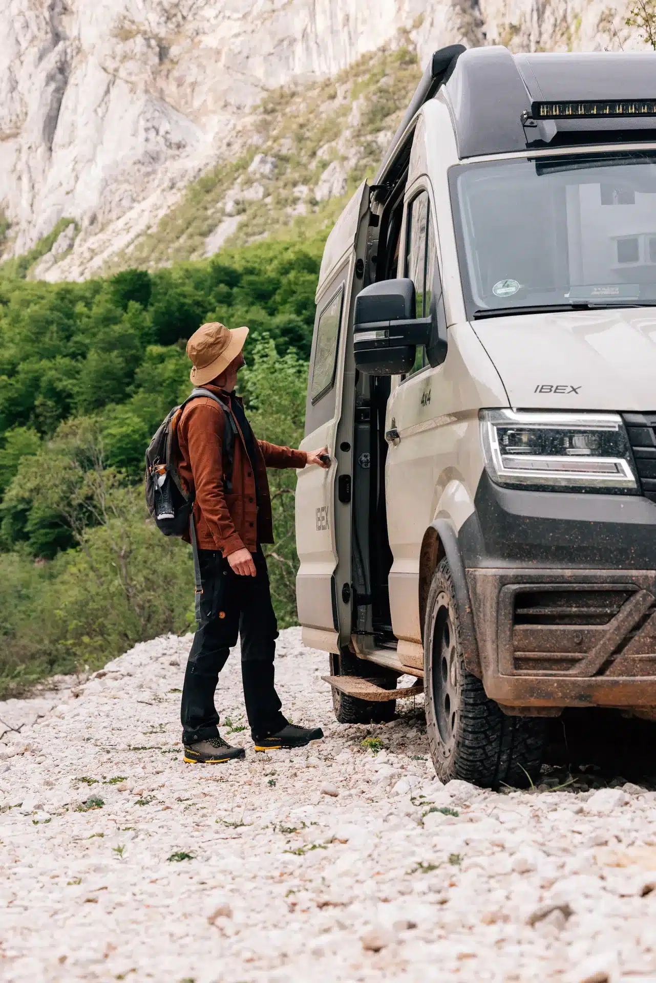 Sunlight IBEX VW 4x4 Camper in hellem Farbton, geparkt im Gelände mit Mann an der Seitentür, umgeben von Felsen und Natur
