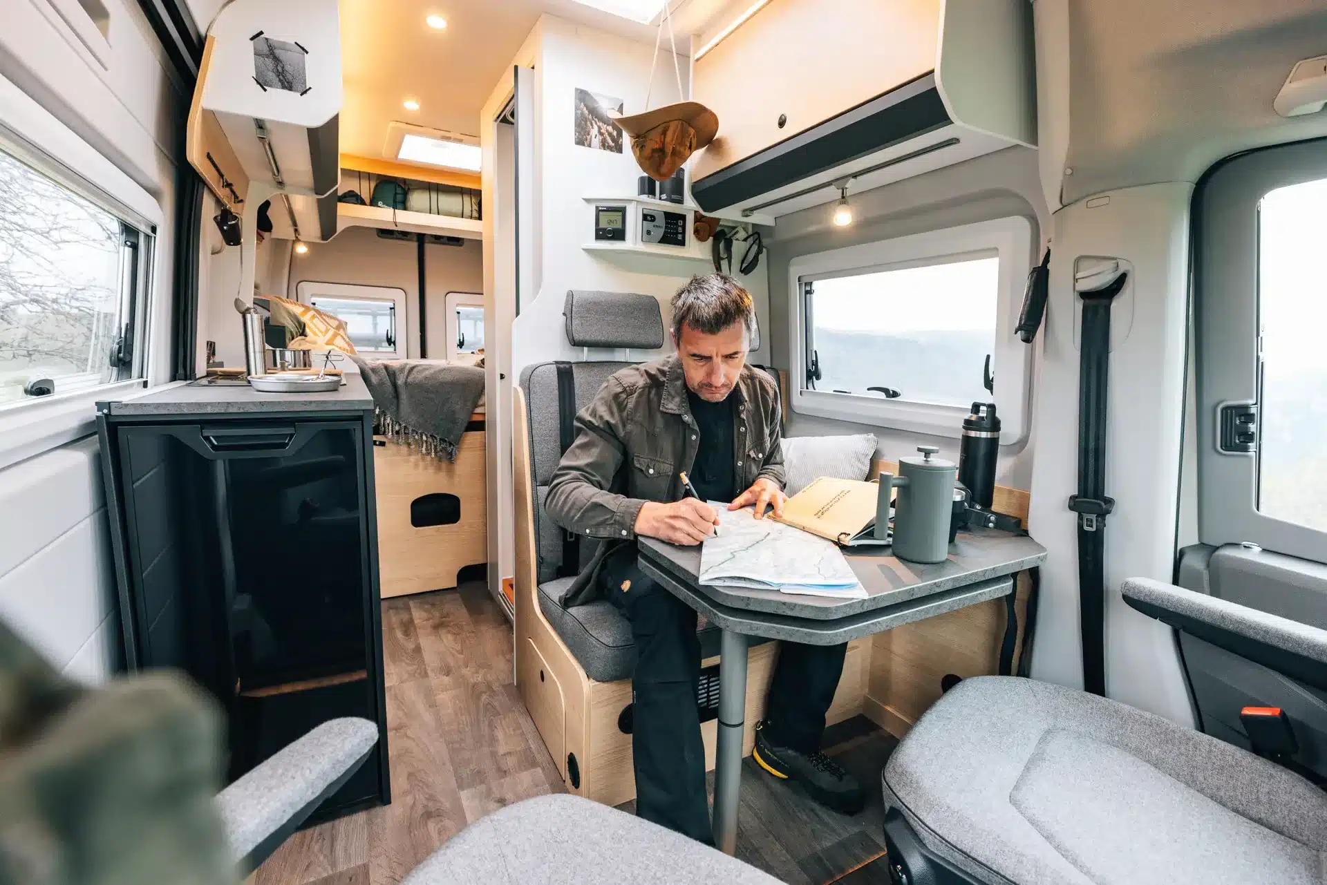 Mann sitzt am Tisch im Wohnbereich des Sunlight IBEX VW Campervans und betrachtet eine Karte, im Hintergrund ist das Bett zu sehen.
