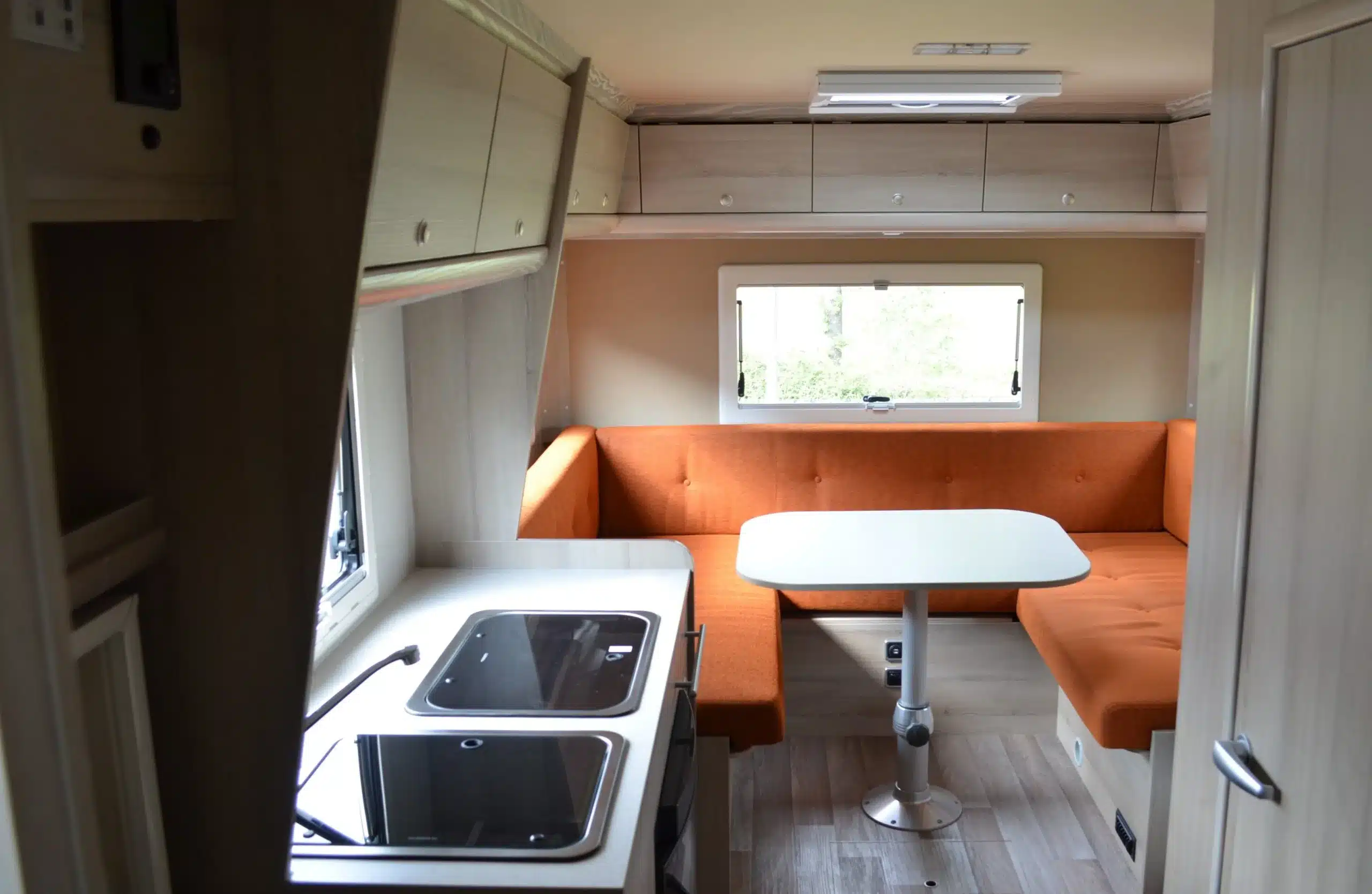 Innenraum des Wohnmobils K 630 HLB mit orangefarbener Sitzgruppe, Tisch und Küchenzeile