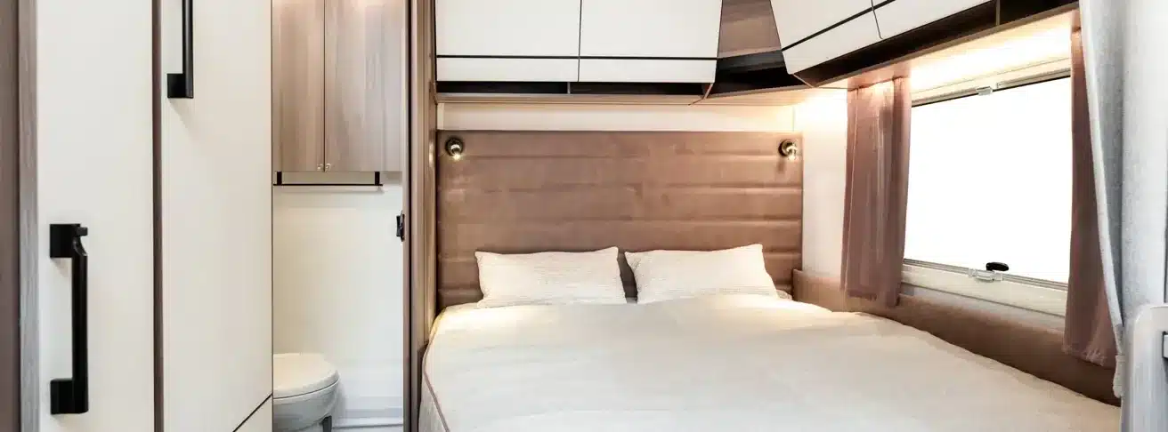 Innenraum des KABE Estate 470 XL mit Doppelbett, Polsterkopfteil, Fenster und angrenzendem Bad mit Toilette