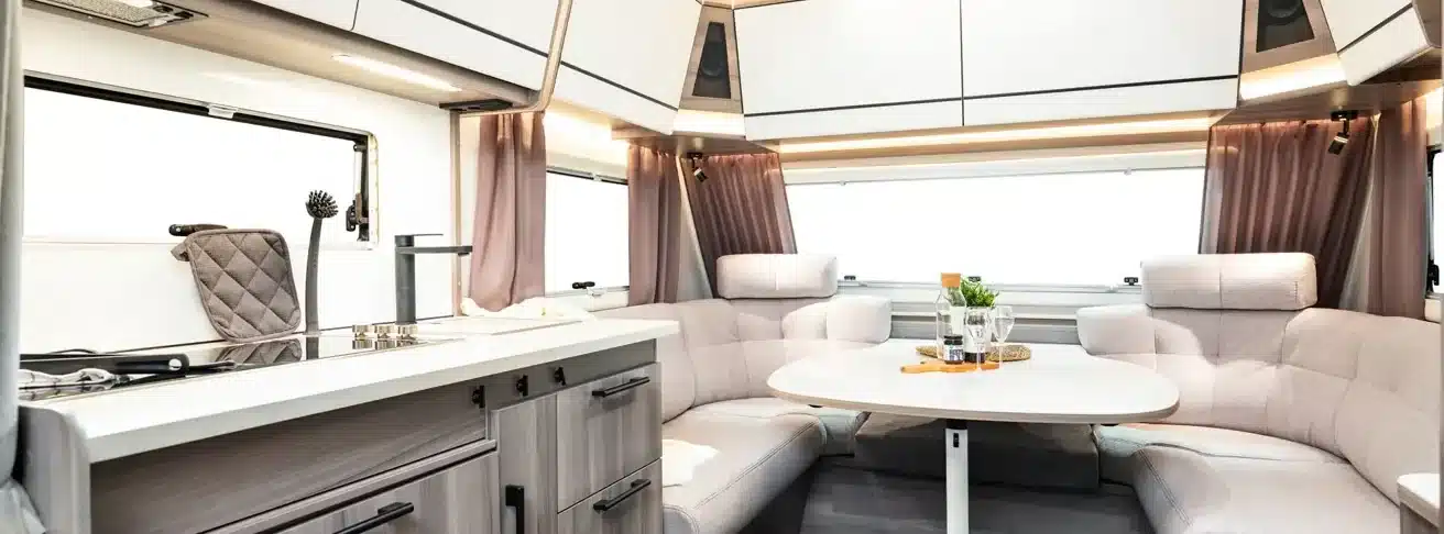 Heller Innenraum des KABE Estate 470 XL mit Küche, Sitzgruppe, Tisch, Polstern und Oberschränken