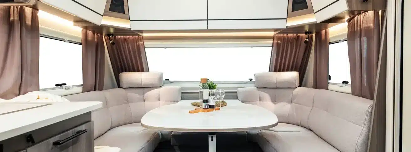 Helle U-förmige Sitzgruppe im Innenraum des KABE Estate 470 XL mit Tisch, Polstern, Fenstern und Oberschränken