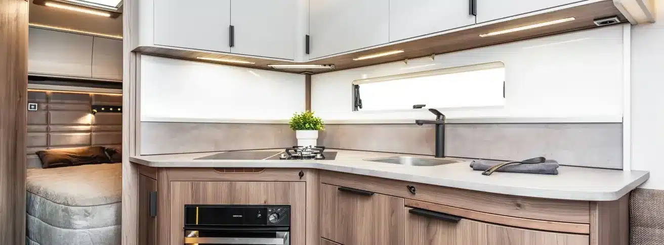 Innenansicht des KABE Royal 600 XL mit moderner Küche, Holzdekor, Spüle, Gaskocher und Schlafbereich im Hintergrund.