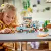 Kind spielt mit dem LEGO Friends Wohnmobil 42663, Spielfiguren, Fahrrad und Campingzubehör auf einem Tisch.
