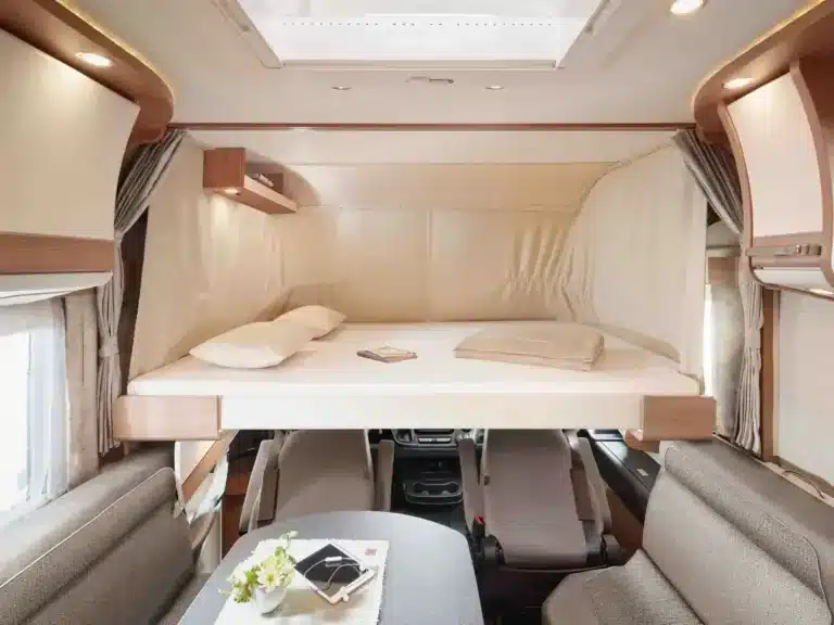 Ausgebautes Hubbett über dem Fahrerhaus eines Malibu Edition+ Wohnmobils mit Sitzgruppe und Schränken
