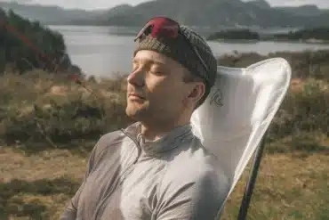 Person entspannt auf weißem Robens Observer Carbon Campingstuhl in naturnaher Landschaft mit See im Hintergrund