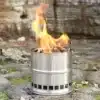 Edelstahl Outdoor-Kocher mit brennendem Holz auf einem Steinuntergrund