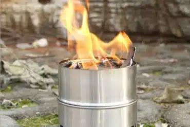 Edelstahl Outdoor-Kocher mit brennendem Holz auf einem Steinuntergrund
