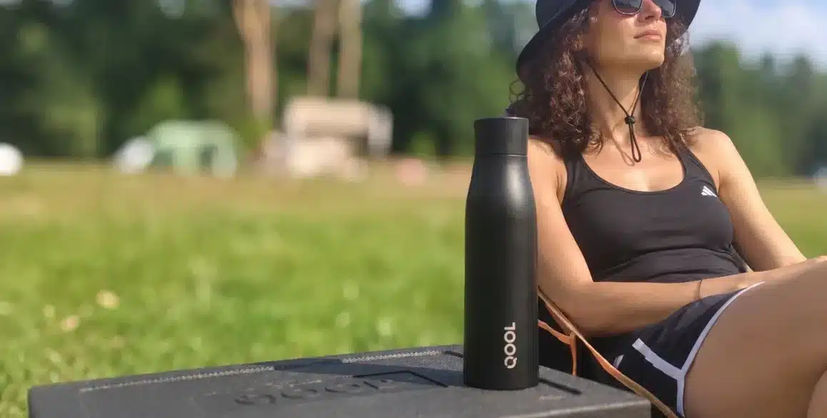Schwarze QOOL Bottle steht neben einer QOOL Kühlbox im Freien