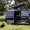 Schwarzer Reimo Van-Concept Campervan mit geöffnetem Aufstelldach auf einer Wiese