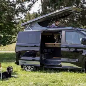 Schwarzer Reimo Van-Concept Campervan mit geöffnetem Aufstelldach auf einer Wiese