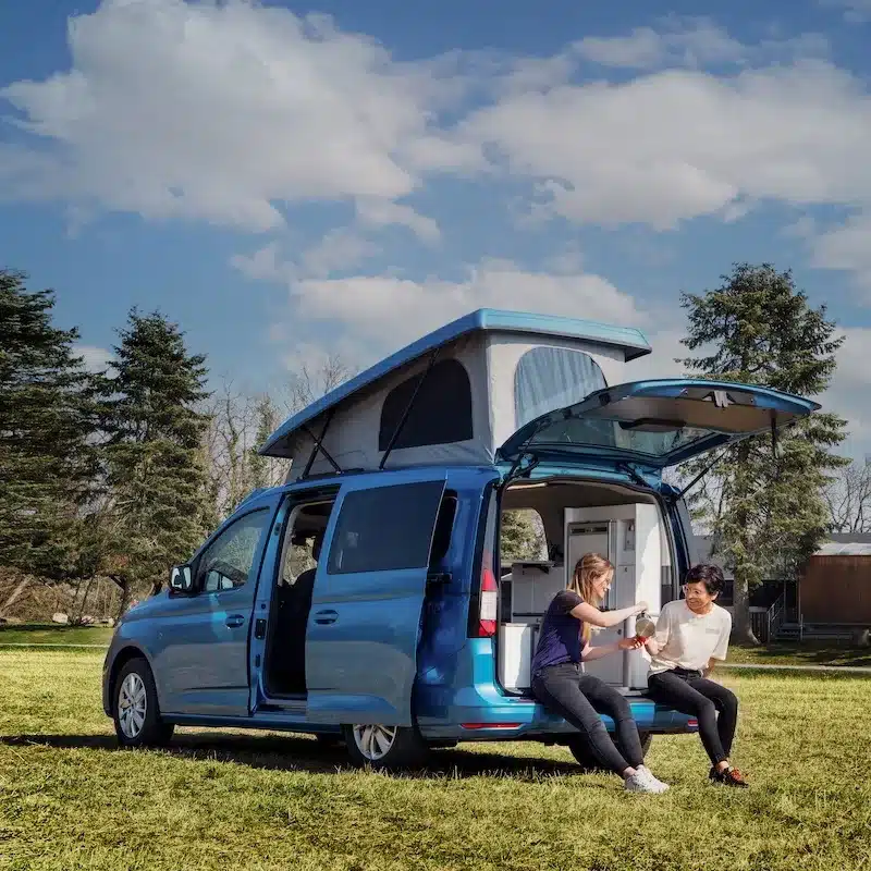 Blauer Campervan mit Aufstelldach, geöffneter Heckklappe und Campingausbau im Freien