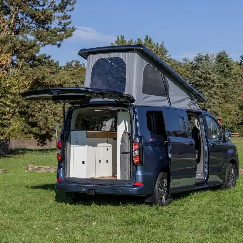 Blauer Campervan des Reimo Van Concept mit geöffnetem Aufstelldach und Heckküche
