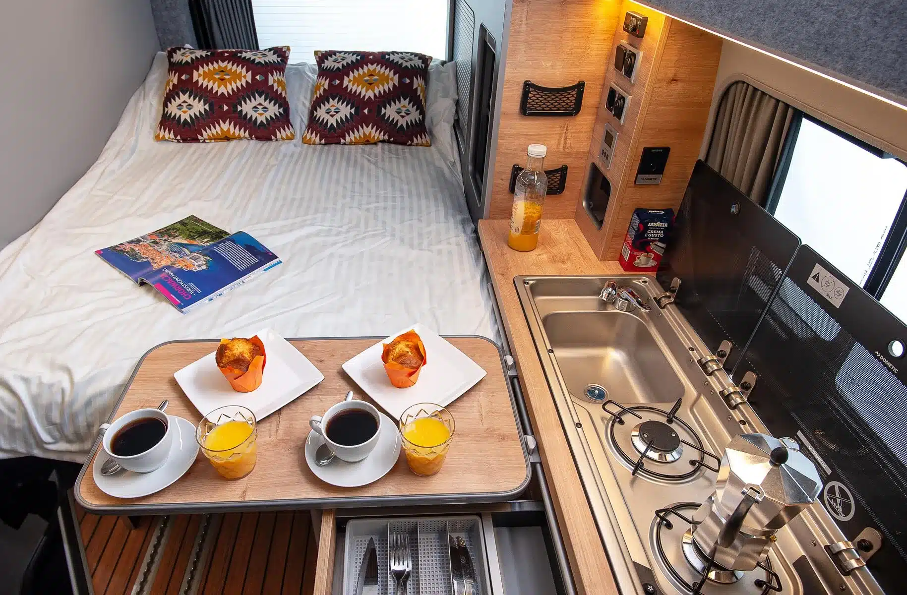 Campervan-Innenraum mit Bett, Küchenzeile, Spülbecken, Gaskocher und gedecktem Tisch