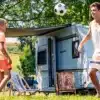 Weinsberg-Caravan mit ausgefahrener Markise und zwei Menschen beim Camping im Grünen