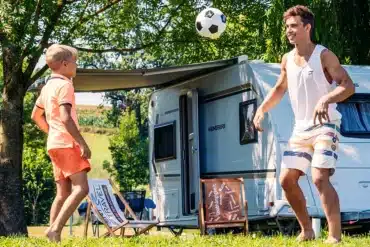Weinsberg-Caravan mit ausgefahrener Markise und zwei Menschen beim Camping im Grünen