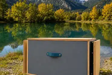 ‚S KISTL Chef Campingbox auf Kiesuntergrund mit Bergen und See im Hintergrund