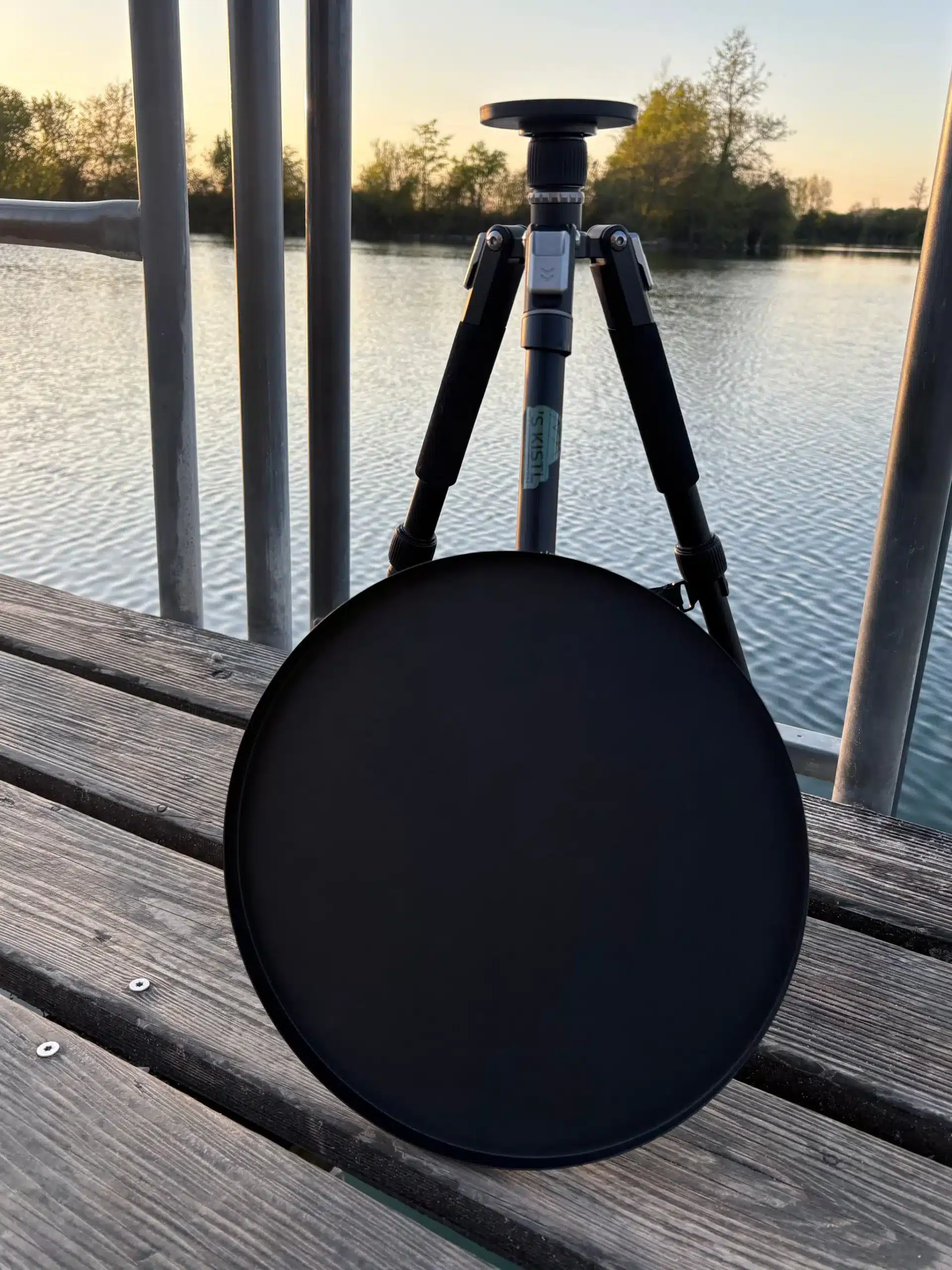 ‘S KISTL magneTISCH Campingtisch aus Aluminium mit runder Tischplatte auf Holzsteg neben einem See.