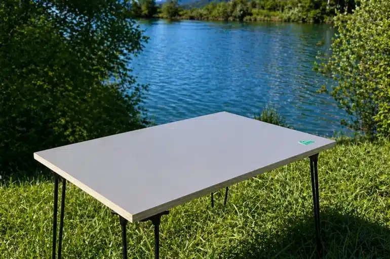 Stabiler, minimalistischer Campingtisch aus Birke Multiplex mit Metallbeinen am Seeufer, im Grünen, vor Alpenpanorama