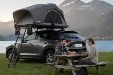 Graues Skandika-Dachzelt mit Leiter auf einem SUV am See vor verschneiten Bergen