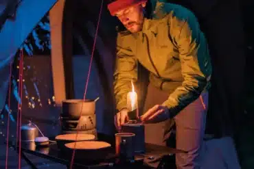Person zündet die Snowdon Gaslaterne auf einem Campingtisch an einem Zelt an