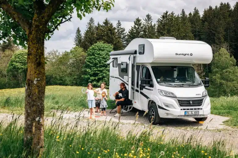 Familie steht und sitzt vor einem Sunlight Alkoven Root A60 Wohnmobil auf einer Wiese