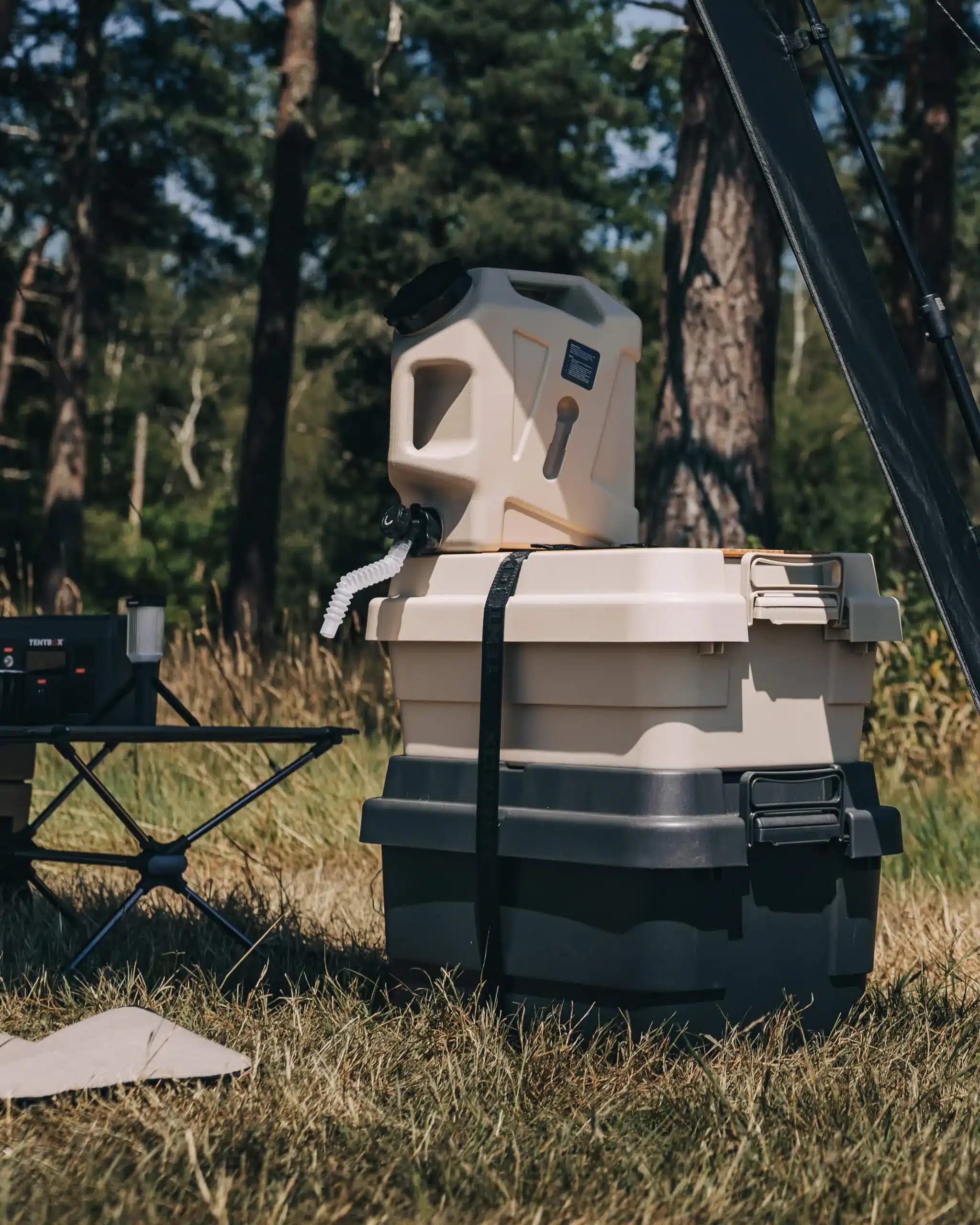 Beiger Camping-Wassertank auf einer Outdoor-Box neben einem Dachzelt im Wald