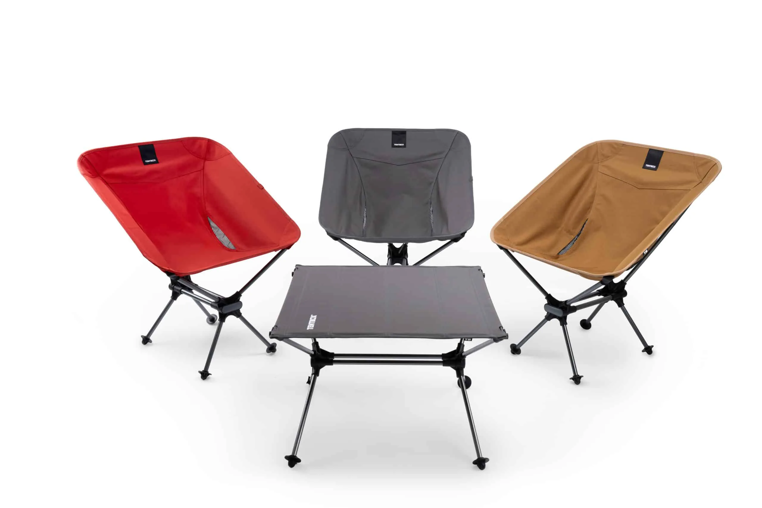 Drei faltbare TentBox Campingstühle in Rot, Grau und Beige neben einem schwarzen Campingtisch