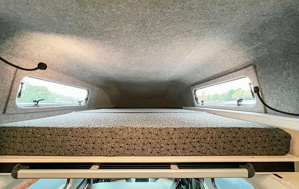 Oberer Schlafbereich mit Matratze und zwei Seitenfenstern im Hochdach eines Campervans
