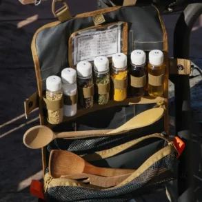 Offene Tool Roll Spice 2 Gewürzrolle mit gefüllten Behältern, Holzkochlöffeln und frischem Gemüse auf einem Holztisch beim Camping.