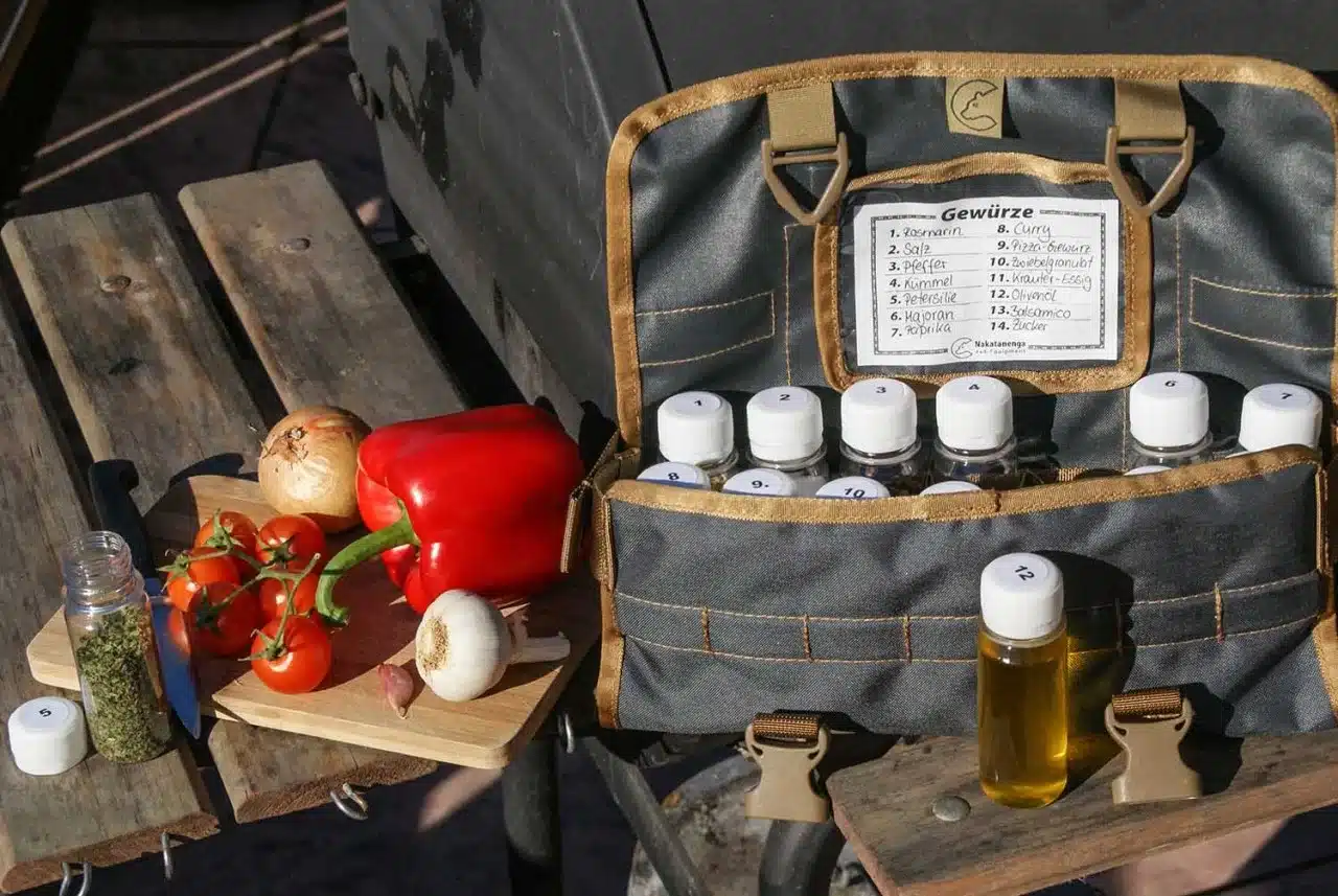 Tool Roll Spice Gewürztasche mit 14 Gewürzbehältern, ausgeklappt auf einem Campingtisch mit Gemüse und Ölfläschchen, Outdoor-Küche im Einsatz