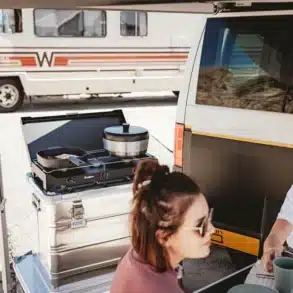 Mobile Campingküche mit Gaskocher und Kochgeschirr neben einem weißen Campervan