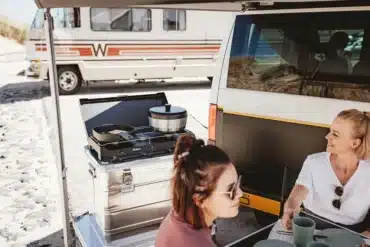 Mobile Campingküche mit Gaskocher und Kochgeschirr neben einem weißen Campervan