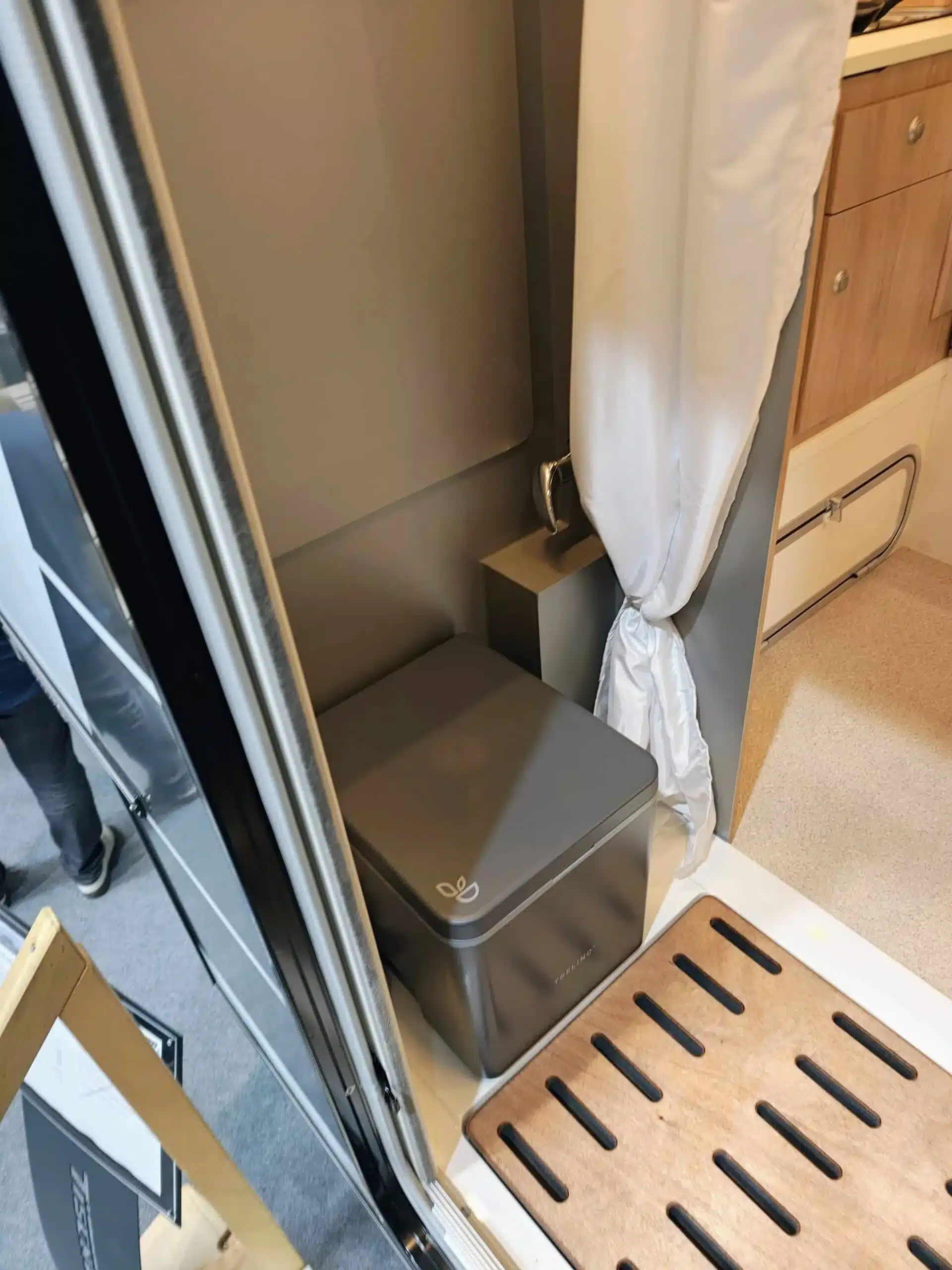 Kompakte Trockentrenntoilette mit geschlossenem Deckel neben einem Vorhang und Holzmöbeln in einer Wohnkabine