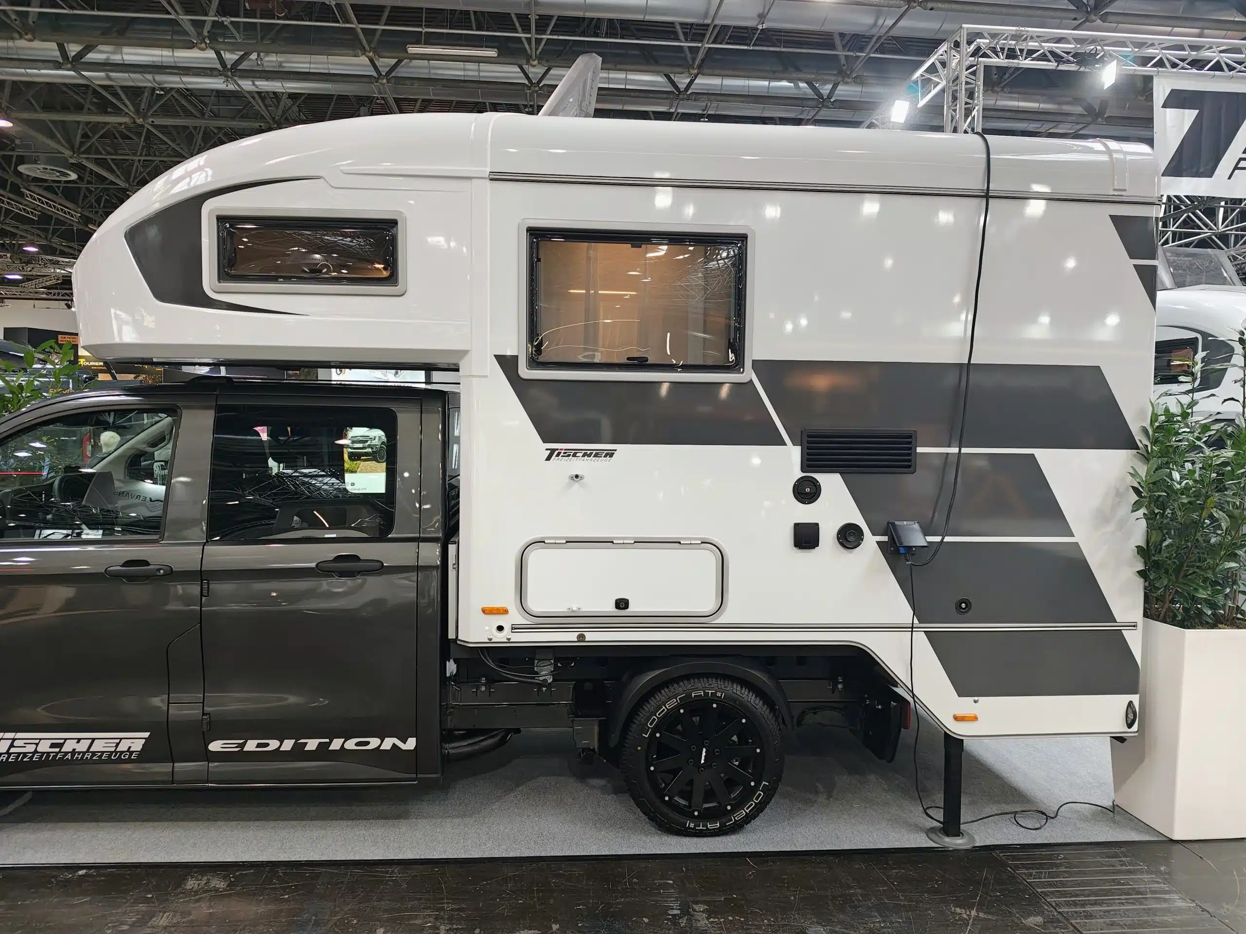 Weiße Tischer Wohnkabine mit schwarzen Designelementen auf einem dunklen Pickup in einer Messehalle