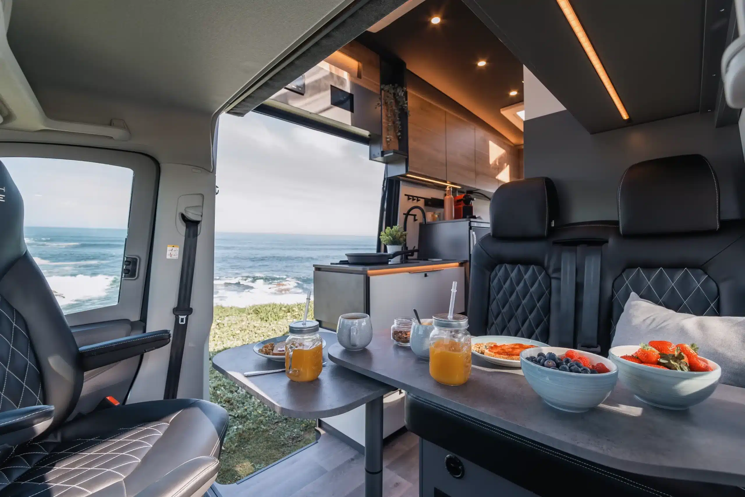 Innenraum eines Campervans mit Sitzgruppe, Küche und Blick auf das Meer