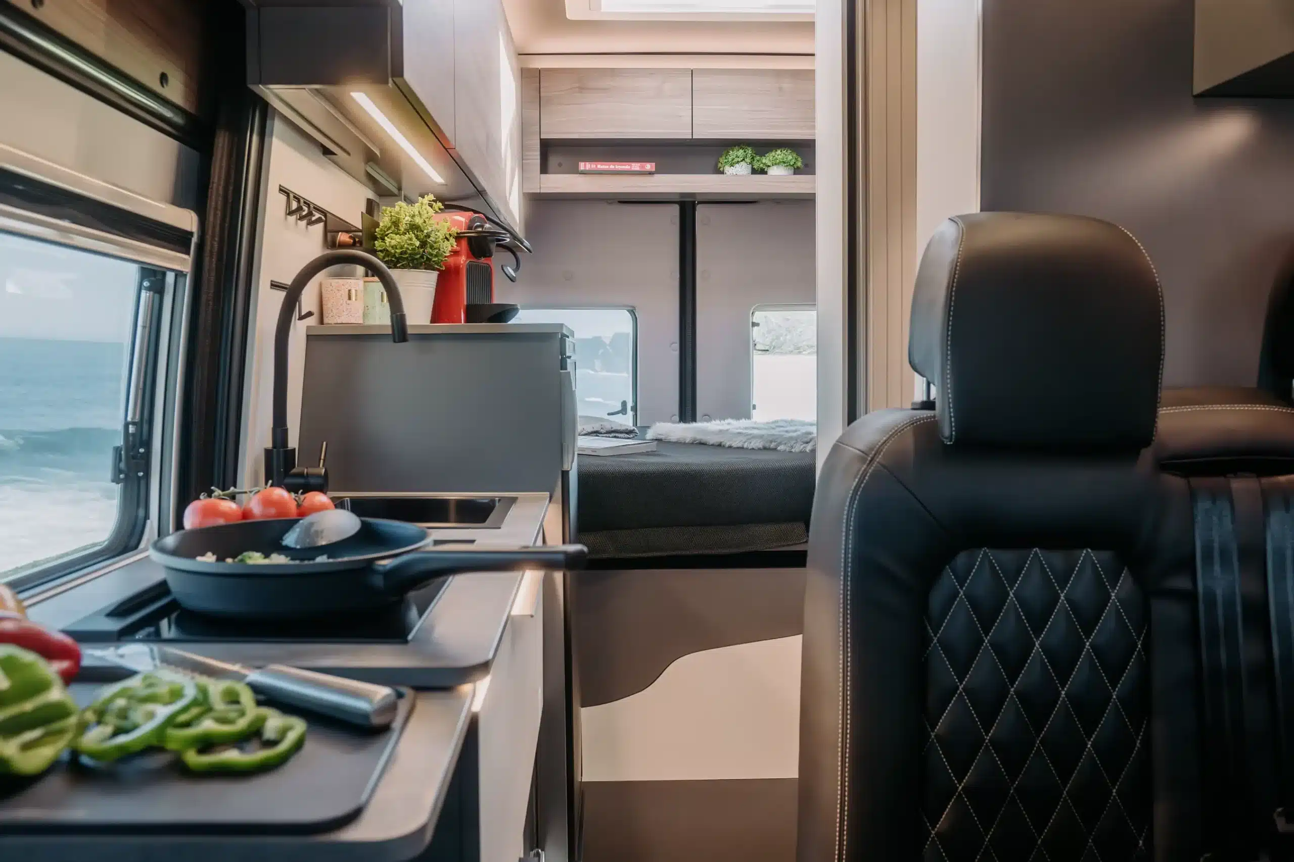 Innenraum eines Campervans mit Küche, Spüle, Kochfeld und Bett im Heck