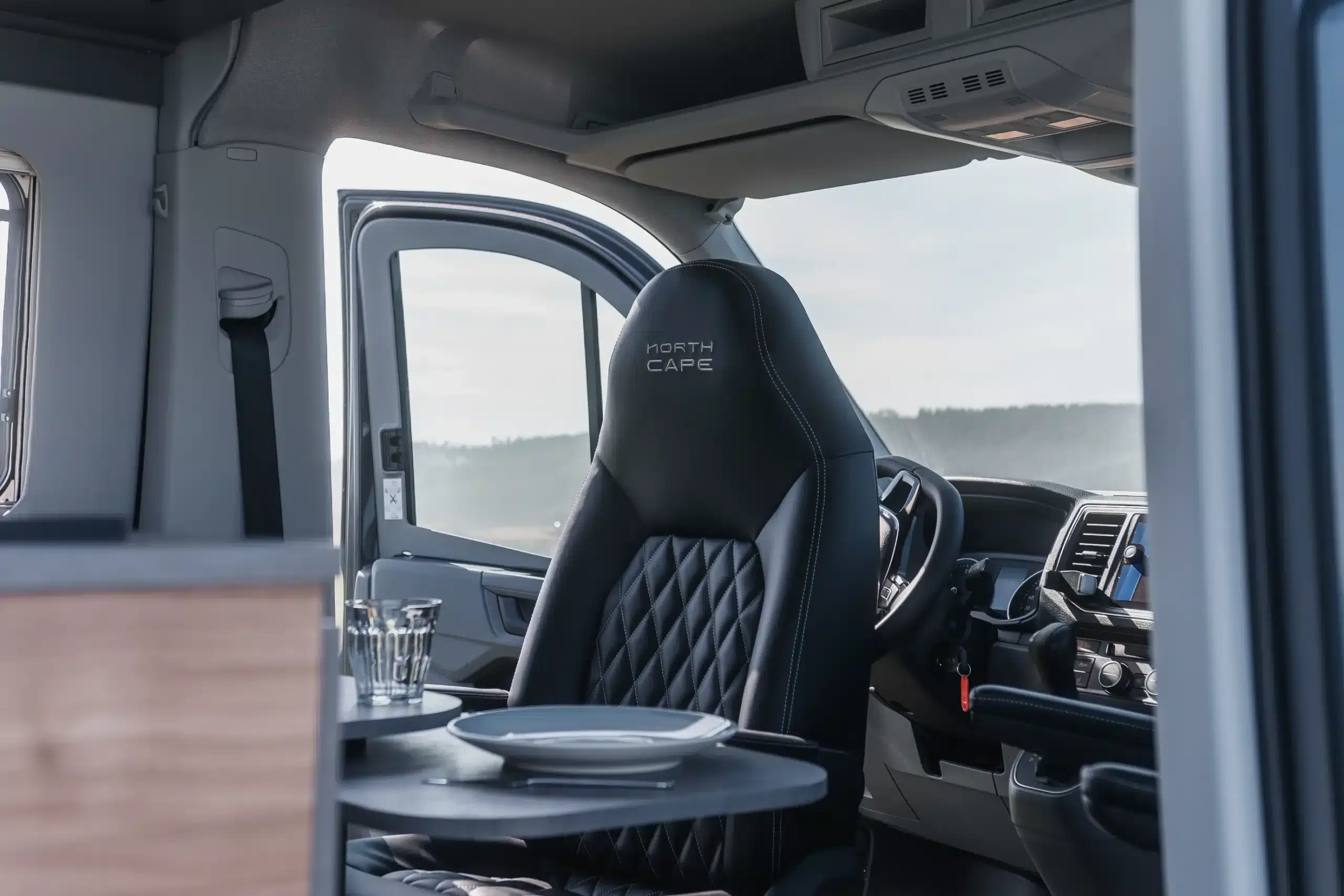 Innenraum des ADVENTURE 6XH Campervans mit schwarzem Fahrersitz, Cockpit und Sitzgruppe