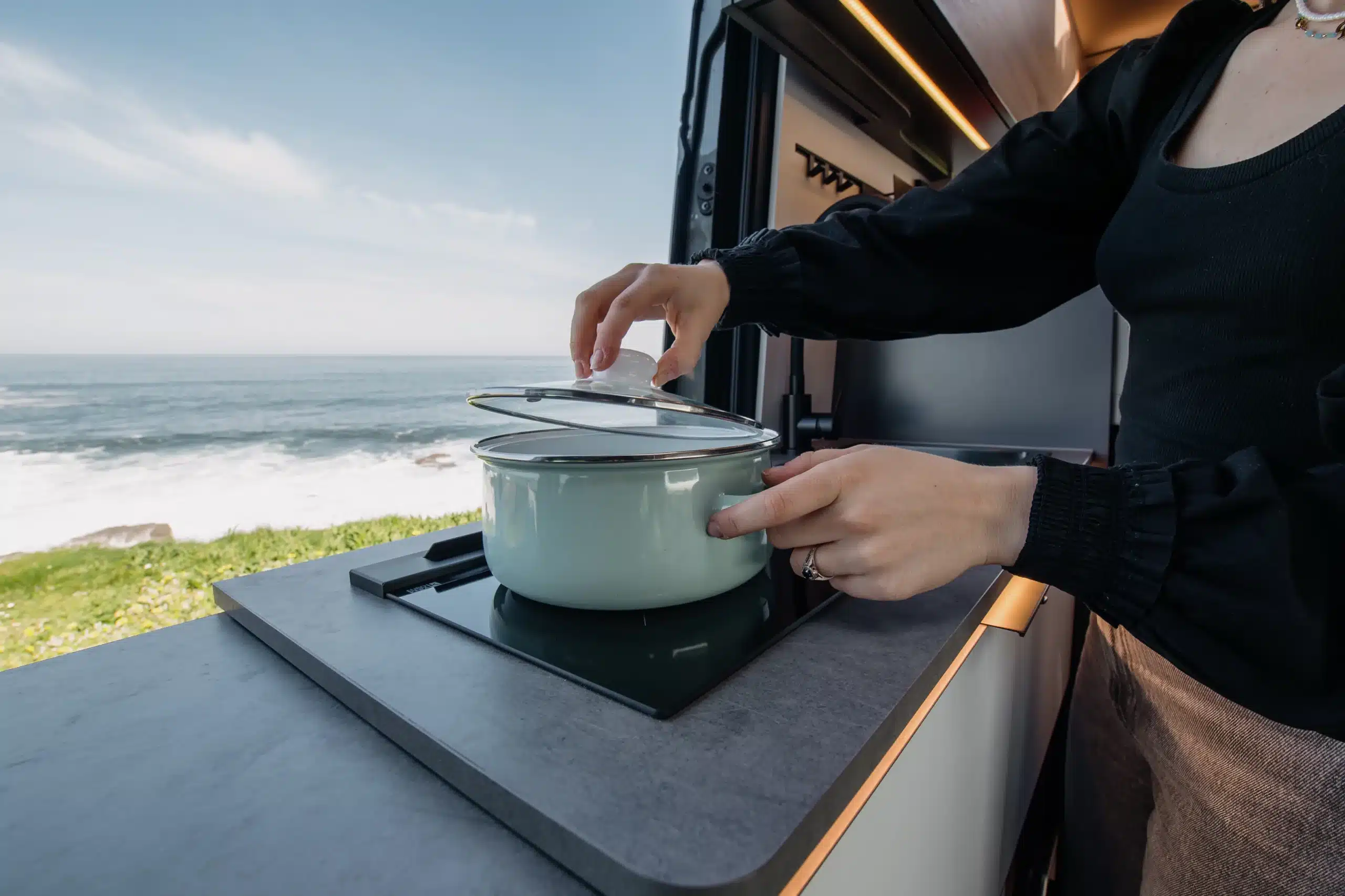 Person mahlt Kaffee mit einer Handkaffeemühle im Innenraum eines Campers