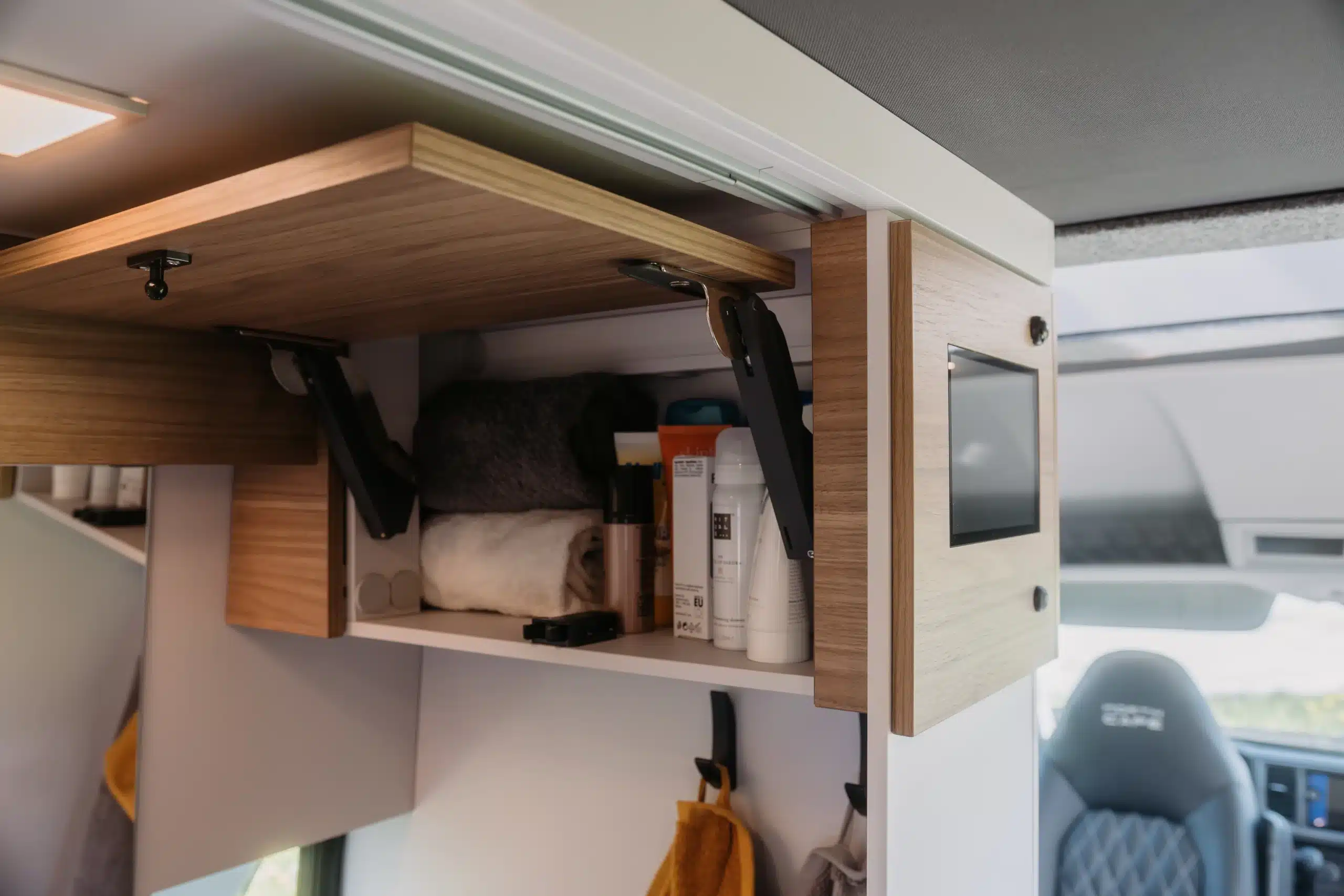 Innenraum eines Campervans mit holzfarbenen Möbeln, Stauraum und Bettbereich