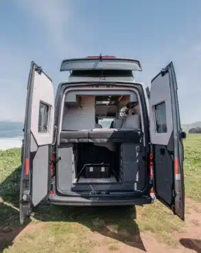 Heckansicht des ADVENTURE 6XR Campers mit geöffneten Türen, ausgeklapptem Hubdach und Schlafbereich