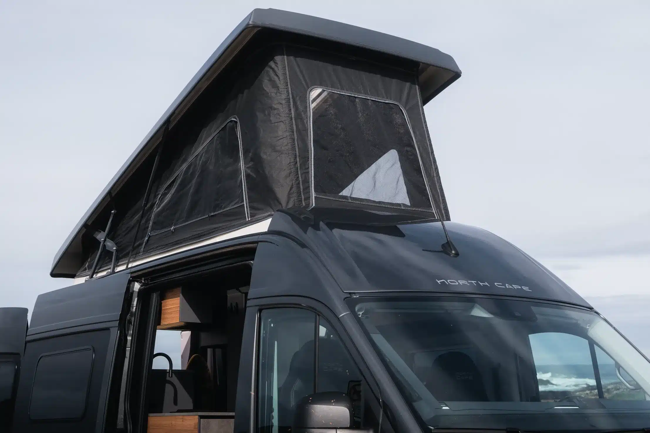 Dunkler Campervan mit geöffnetem Hubdach und seitlich geöffneter Schiebetür
