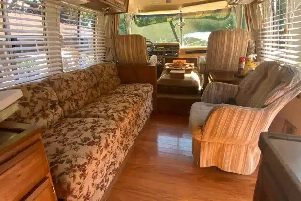 Innenraum eines Airstream 290 Motorhomes von 1985 mit floralem Sofa, Sesseln, Holzfußboden und Cockpit