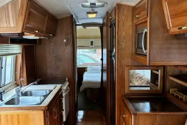 Innenraum eines Airstream 290 Motorhomes von 1985 mit Holzschränken, Spüle, Mikrowelle und Schlafbereich