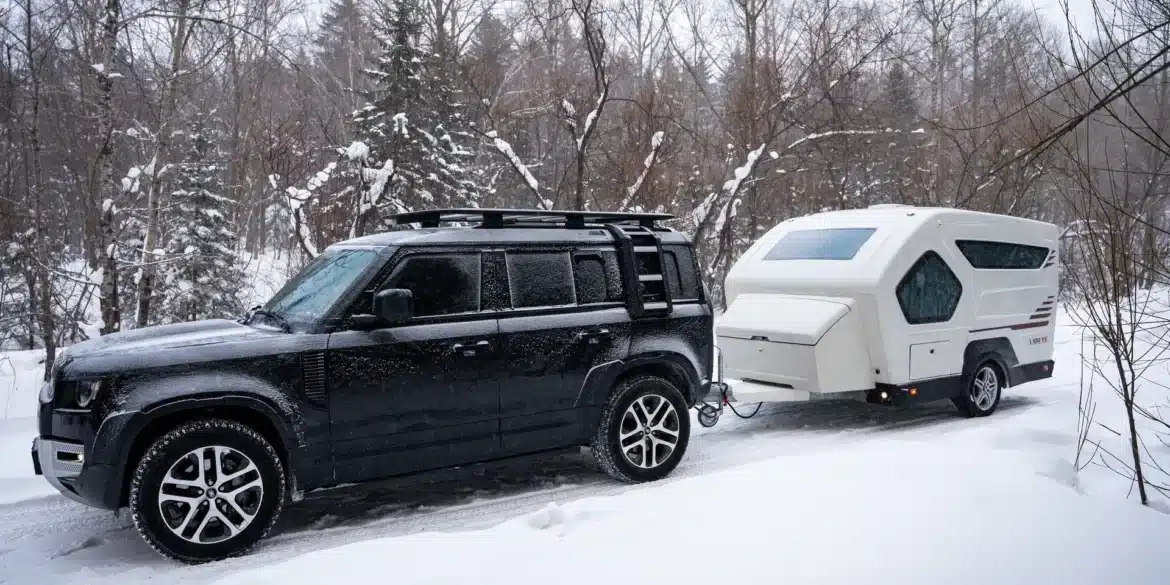 Weißer LIDU RV AQUILA-360 Wohnwagen hinter einem schwarzen SUV im verschneiten Wald