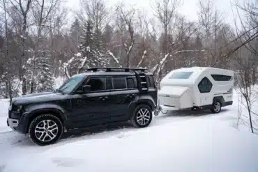 Weißer LIDU RV AQUILA-360 Wohnwagen hinter einem schwarzen SUV im verschneiten Wald