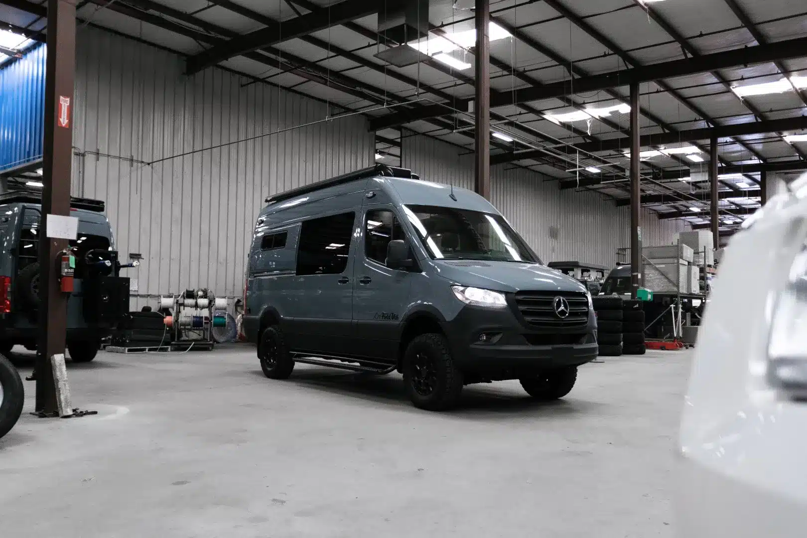 Blau-grauer Mercedes-Benz Sprinter 4x4 als ausgebauter Field-Van-Camper in einer Werkhalle